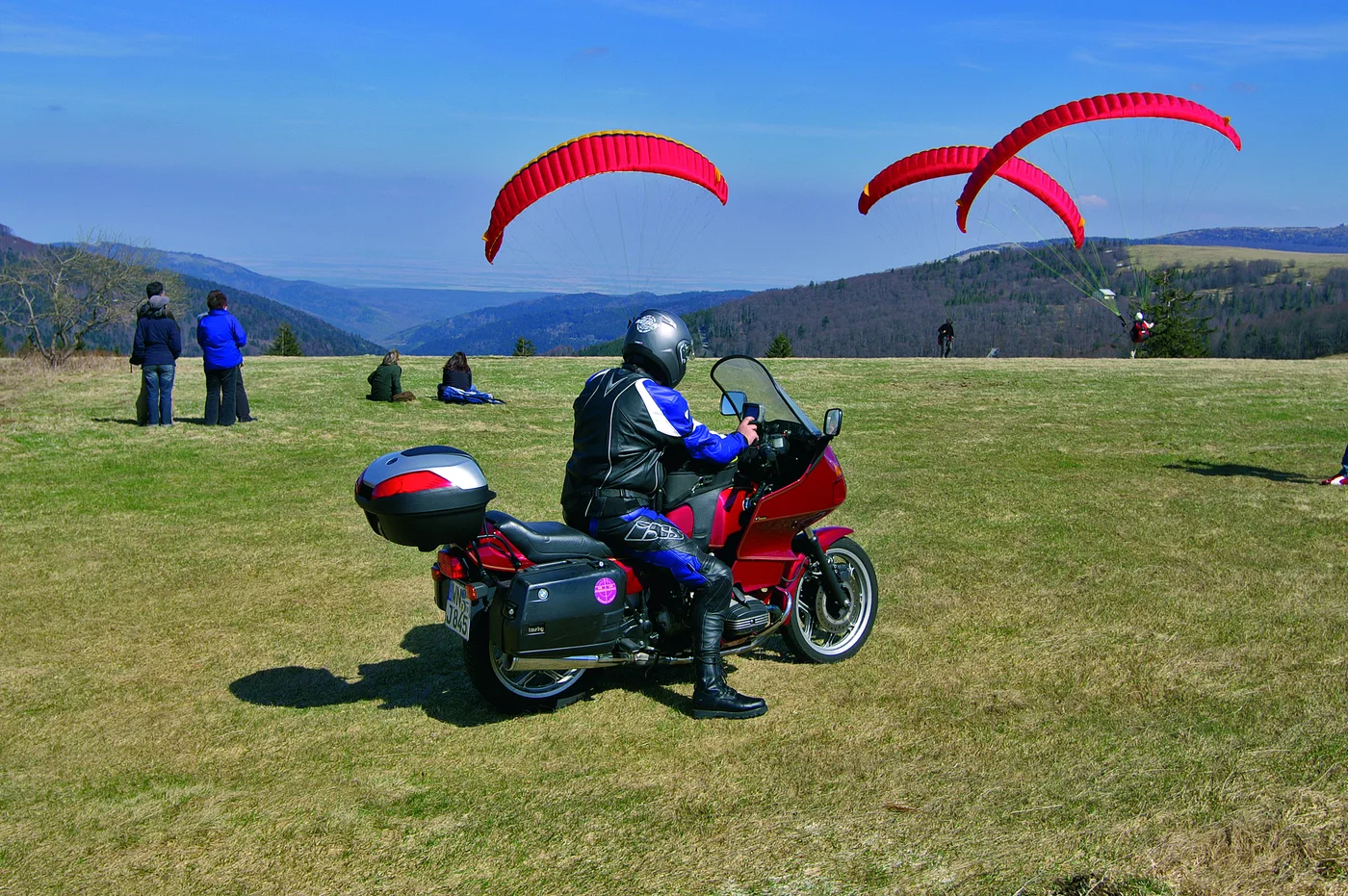 Gleitschirme über der Bergwiese an der Route des Crêtes, davor ein Motorrad